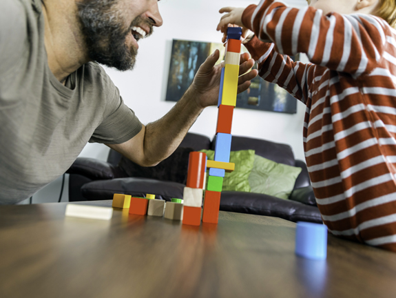 Photo for illustrative purposes only showing a small child building a tower with blocks with an older man helping them
